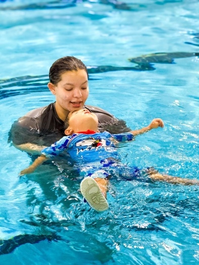A female swim instructor guides a child on their back in a pool. Enroll your child in swim lessons at RAFC. 