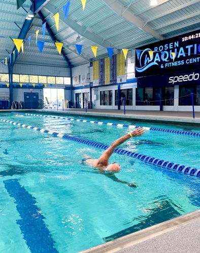 A man with white hair swimming in the lane of a large indoor pool.