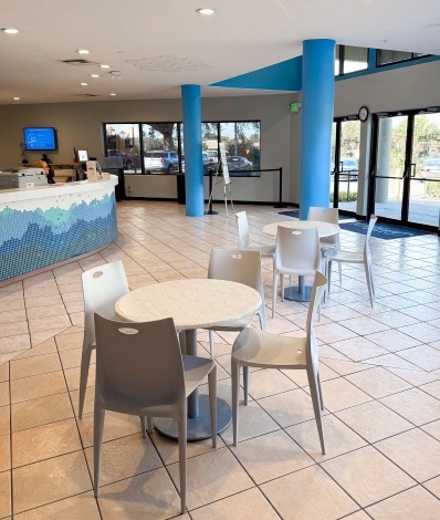 A large lobby with round tables and chairs, blue columns, and a front desk with blue tiling. 