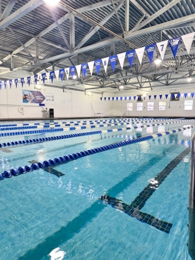 A large indoor pool with lane dividers and a string of blue and white flags hanging overhead.