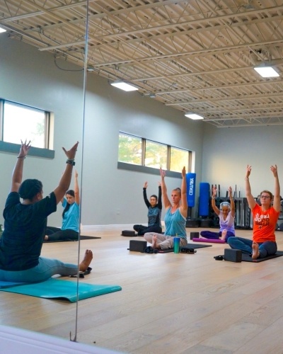  A mirror reflecting a group of people sitting on yoga mats with their arms raised in the air. 