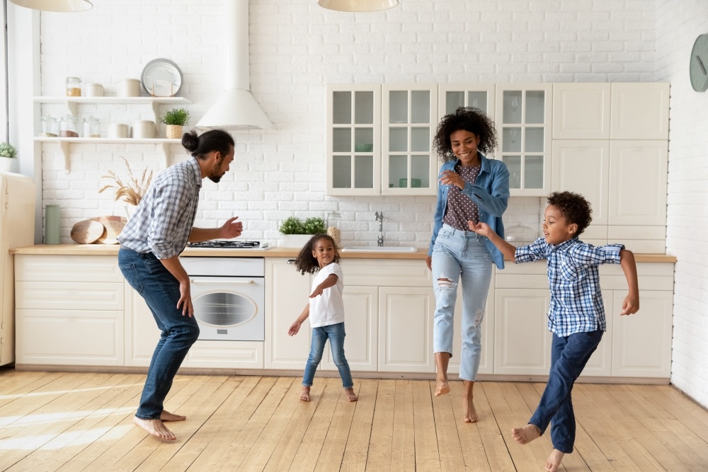 A mom, dad, and two kids dance together in a bright kitchen. 