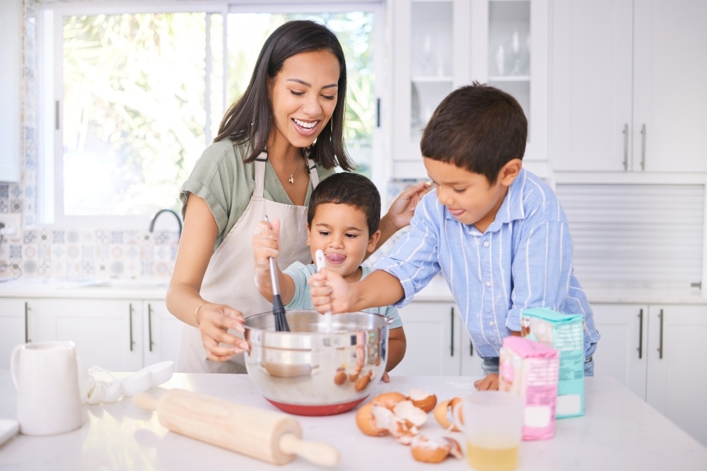 A mom and her two sons stir a bowl as they bake together in the kitchen, one of our healthy activities for moms to do with kids. 