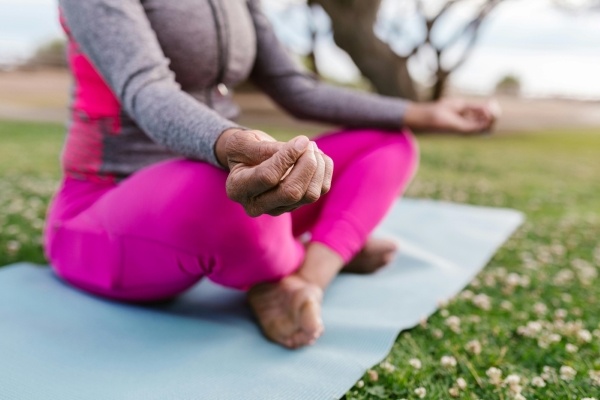 A close-up of a woman's hands as she sits cross-legged on a yoga mat in a field of clover.