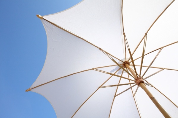 A view of an outstretched white umbrella against a clear blue sky from below.