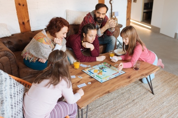 A mom, dad, and three daughters sit around a wooden coffee table playing a board game together.