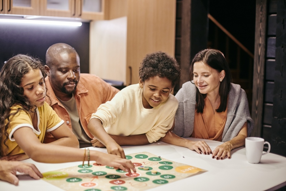 A family of a mom, dad, and two kids sit around a table playing a board game. 