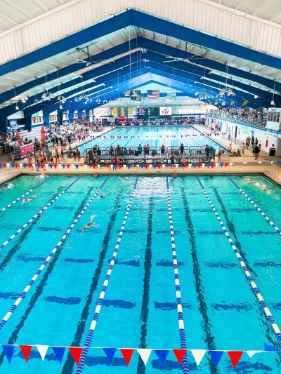 An overhead view of the RAFC pools with blue and white lane markers, red white and blue flags, and swimmers racing in the pool.