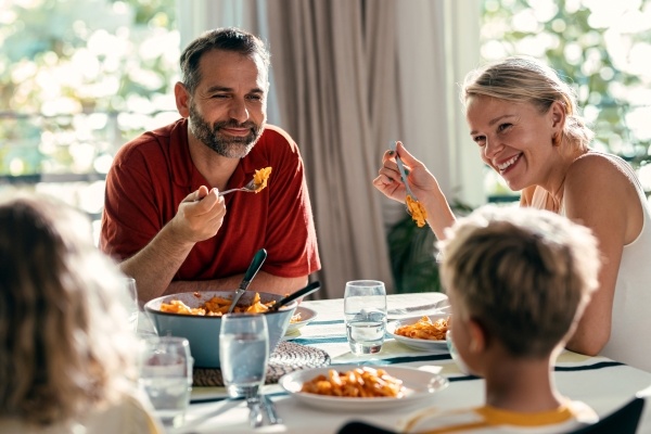 A mom, dad, and two kids sit around a sunny table sharing a meal.