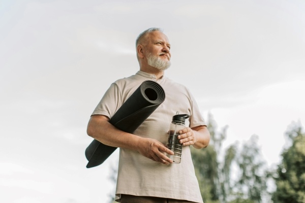 An older man holding a yoga mat and a water bottle.