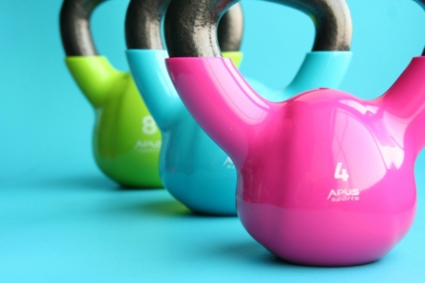 A bright pink, blue, and green kettlebell against a teal backdrop.