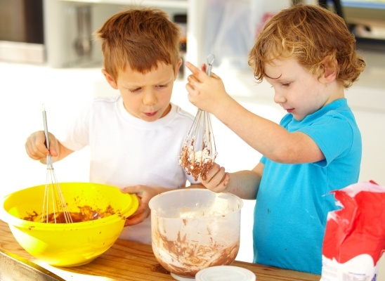 Two toddler boys mix in bowls together with whisks. 
