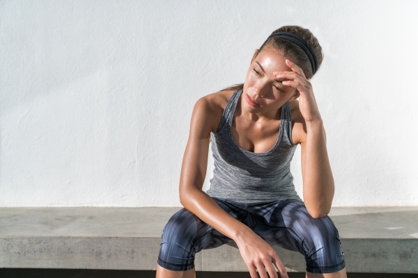 A woman in workout gear sitting on a cement bench rests with her head in her hands.