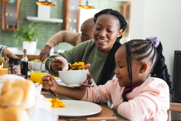 A mom serves her daughter sweet potatoes at a family meal.
