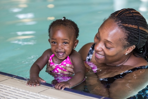 A mom and her daughter hover at the edge of an indoor pool.