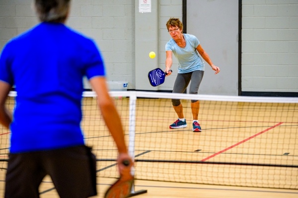 An older man and woman playing pickleball in an indoor pickleball court.