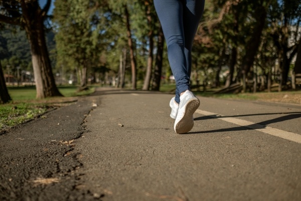 A woman running on a trail in white sneakers and leggings.
