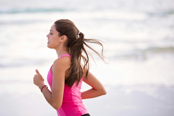 A woman in a pink tank top running on a beach.