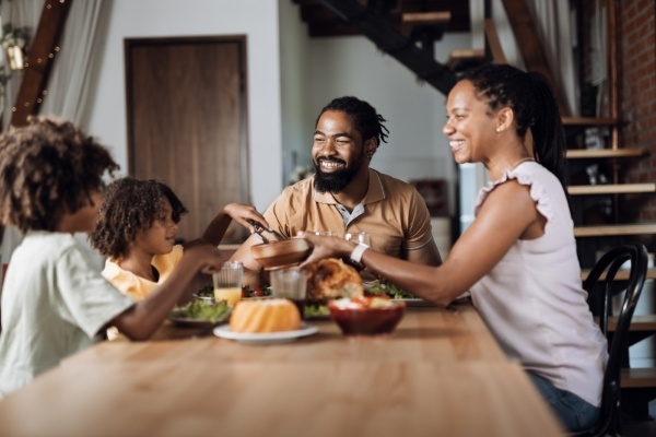 A family with two children is gathered around a table for family dinner, passing food and smiling.
