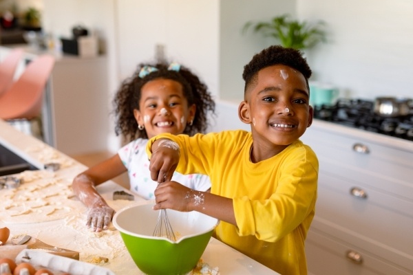 A boy and girl with flour on their faces stand at a counter with baking equipment, smiling.