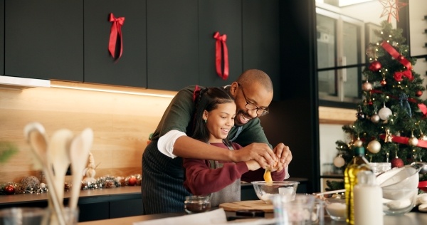 A dad and daughter enjoy Christmas baking together in a house decorated for the holidays.