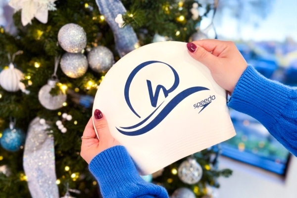 Hands hold a white baseball cap with the RAFC logo in front of a decorated Christmas tree.