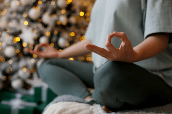 A woman practicing yoga and meditation in front of a Christmas tree.
