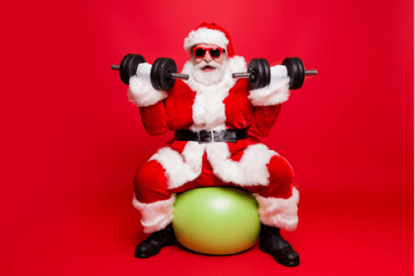 A man dressed up as Santa doing a workout with free weights and an exercise ball.