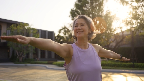An older woman in fitness clothes practices yoga outdoors, a great exercise for physical and mental health.