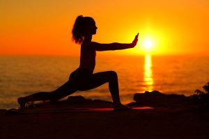 Tai chi versus yoga - a woman practicing tai chi during a sunset at the beach
