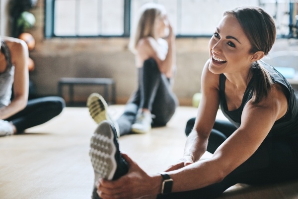 A woman stretching on the floor and smiling in an indoor fitness class.