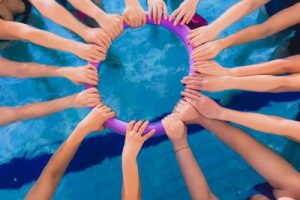 Women training in aqua aerobics learn to swim circle, team hands.