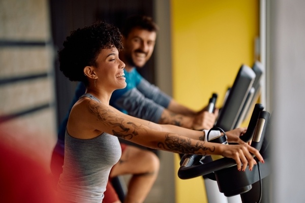 A smiling couple in athletic clothing workout side by side on cardio machines. A couples workout is a fun way to exercise.