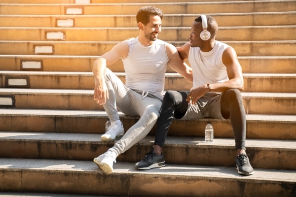 Two men in athletic clothing sit on cement steps, embracing one another.