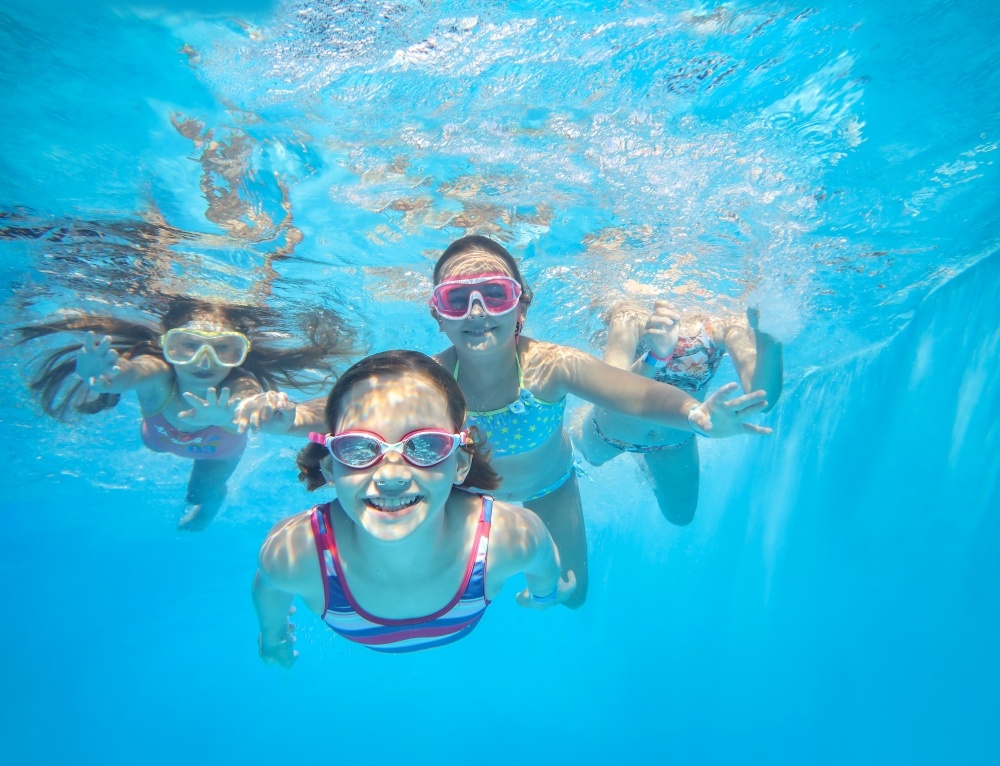 Four kids with goggles swimming underwater.