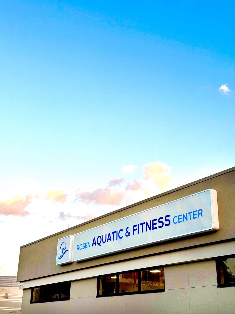 An exterior shot of the Rosen Aquatic & Fitness Center sign against a blue sky with pink clouds.