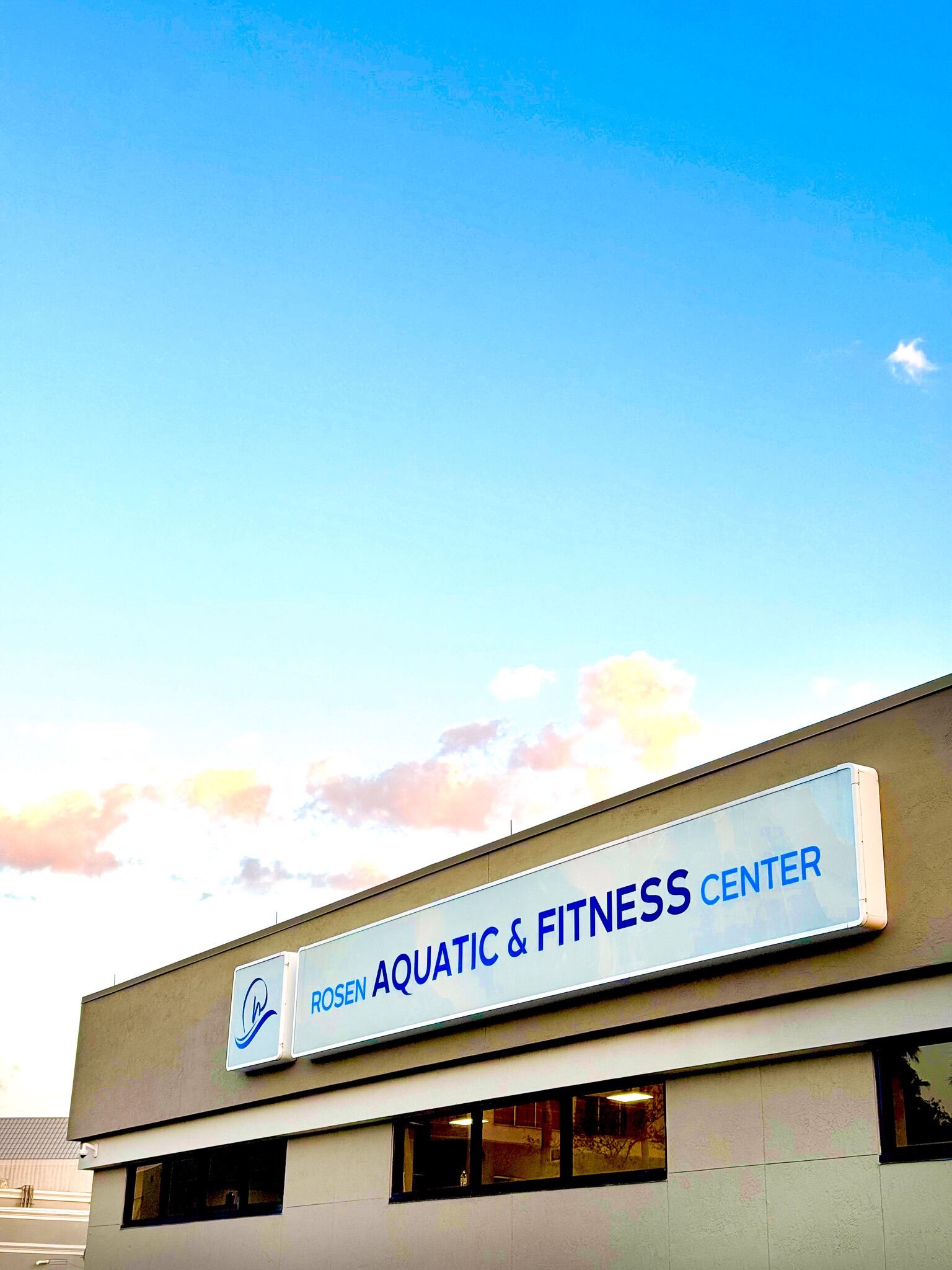 An exterior shot of the Rosen Aquatic & Fitness Center sign against a blue sky with pink clouds.