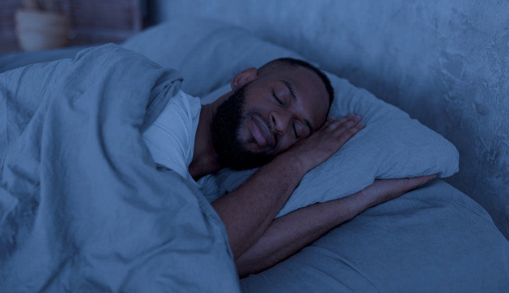 A man sleeps on his side in a dark room. 