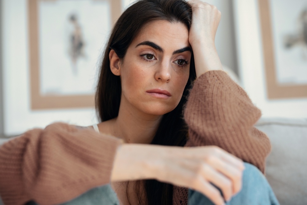 A woman in a sweater sits with her head in her hand, looking tired and stressed. 