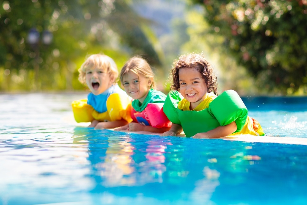 Three kids in colorful arm floaties in a swimming pool.