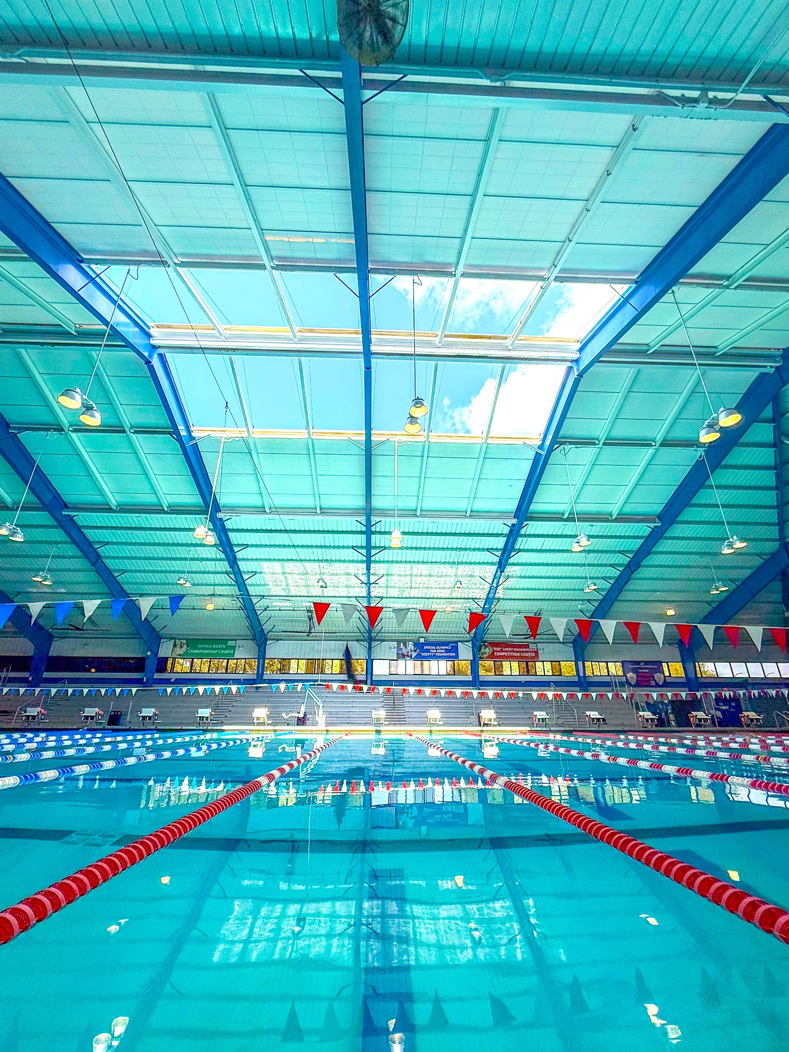 A large indoor swimming pool at Rosen Aquatic & Fitness Center with lap lanes, hanging flags, and a large skylight overhead.