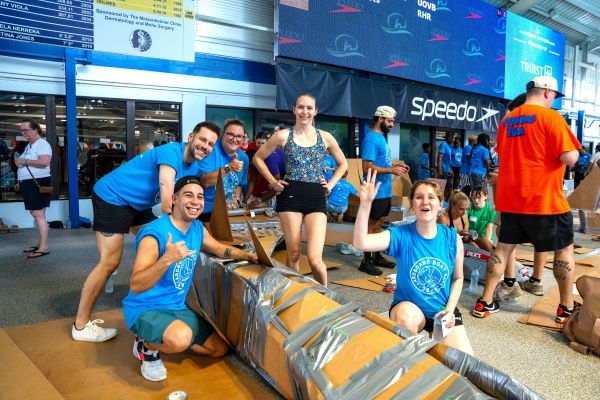 A team in blue t-shirts poses with their cardboard boat at the RAFC Cardboard Boat Race.